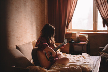 Teenage girl playing guitar while sitting on bed at home