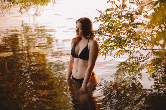 Young woman in bikini standing in water at sunset