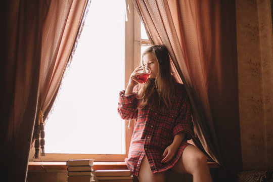 Young woman drinking tea while sitting on window sill at home