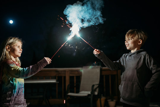 Boy and girl holding sparklers against dark sky