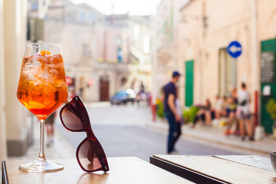 Glass of Aperol Spritz cocktail over Matera streets background