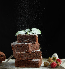 stack of square baked brownie chocolate cake slices sprinkled with white sugar