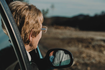 A old woman with her head out the window enjoying a scenic drive