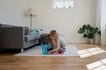 Young blonde boy playing with an digital tablet at home