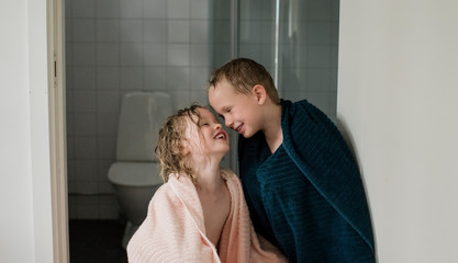 Girl and boy standing outside a bathroom in towels laughing and playing