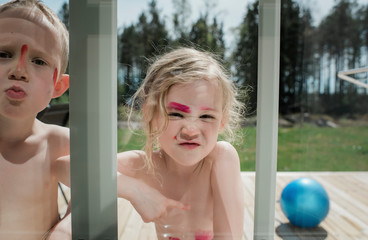 Young girl making faces through a window with paint on her face