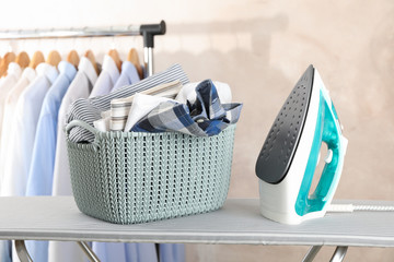 Basket with clean laundry and iron on ironing board, space for text - obrazy, fototapety, plakaty