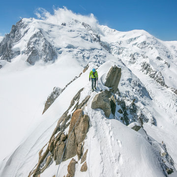 A male alpinist heads across an exposed knife-edge ridge on Mont Blanc