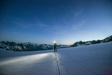 An alpinist uses a headlamp to navigate glaciated terrain pre dawn