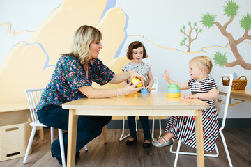 Teacher begins to hand toddler girl a piece to her stacking toy