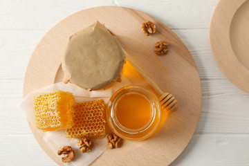 Honeycombs, walnuts, dipper and jars with honey on wooden background, top view