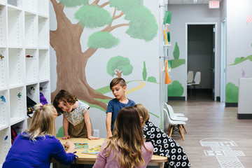 Kids stand around a table with teachers and puzzles