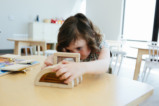 Little girl sits at table with toy and examines toy closely