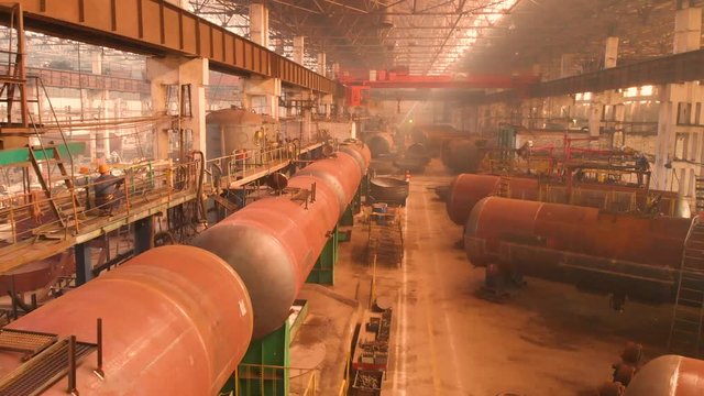 Slow flight inside the factory for manufacturing railway trains with wagons. Workers weld metal blocks and move wagons around the factory