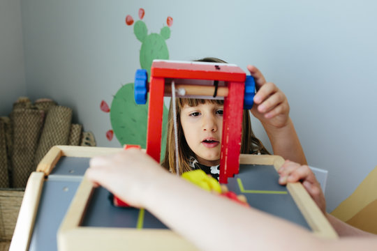 Little girl cranks wheel on a wooden toy