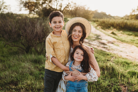 Portrait of happy young mother and children smiling in backlit meadow - Powered by Adobe