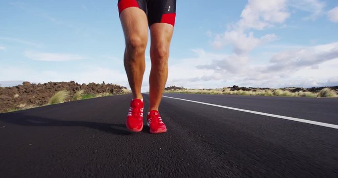 Running shoes on male triathlete runner - close up of feet running on road. Man jogging outside exercising training for triathlon ironman. REAL TIME on RED Cinema Camera.