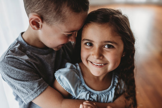 Portrait of young girl while brother embraces her and laughs
