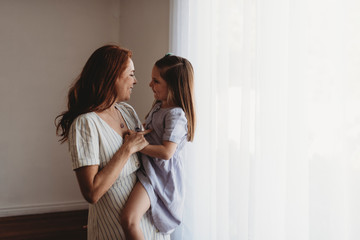 Side view of young mother holding young daughter and smiling at her