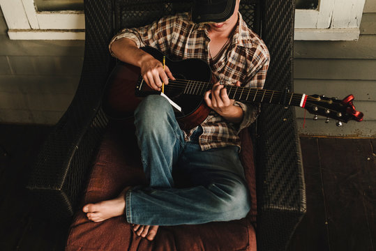 Teen boy plays guitar and writes song on front porch