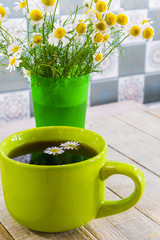 Black tea in a green cup on a wooden background and chamomile