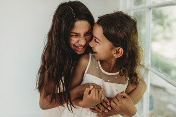 Sisters hugging in natural light studio while looking at each other