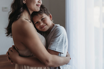 School-aged son being embraced by mother in natural light studio