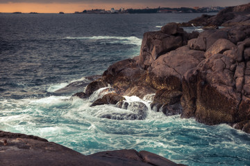 Fototapeta na wymiar Rocky beach with sea waves crashing on the rocks and dramatic sunset sky scenery in Sri Lanka