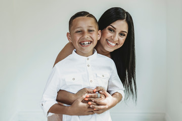 Portrait of mother hugging son from behind and smiling in studio