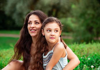 Beautiful young mother embracing and talking with her cute surprising daughter on summer green grass background in sunny day.