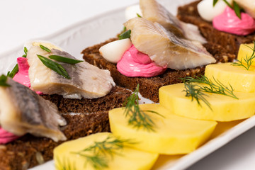Traditional Russian Food: Potatoes and herring with black bread on white plate.