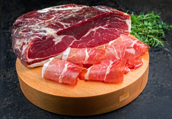 Traditional dry cured and smoked ham with a bouquet garni offered as closeup on a modern design cutting board