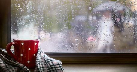 Autumn season background, red cup with hot drink and wet autumnal window