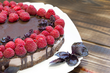 Heart-shaped vegan cake topped with chocolate and raspberries. Delicious healthy homemade dessert. Wooden table with copy space.