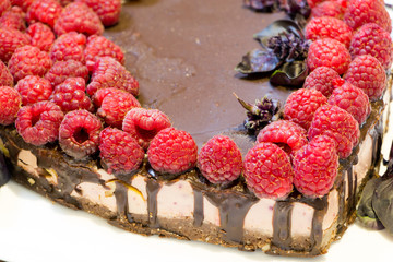 Vegan sweets. Delicious dietary food. Close up chocolate cheesecake with raspberries on white plate with basil leaves.