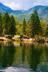 Fototapeta na wymiar Scenery with camping of RV caravan trailers at Bohinj Lake, Slovenia. Nature and camper motorhomes in Slovenija. View of motor home van and green forest. Landscape in summer. Alpine Alps mountains