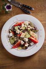 Tomato, cucumber, lettuce and mushroom salad with feta cheese, walnuts and grapes on white plate, wooden table