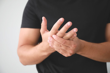 Young man suffering from pain in wrist on light background, closeup
