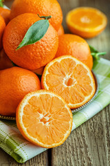 Ripe Mandarin fruit peeled open and place on old rustic look timber with group of mandarin fruits and leaves out of focus on the background