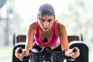 Foto op Plexiglas Beautiful Asian woman exercising on stationary cycling machine in indoor fitness gym, determination face. Sport recreational activity, people workout, or healthy lifestyle concept © Urbanscape