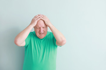 Senior man suffering from headache on light background