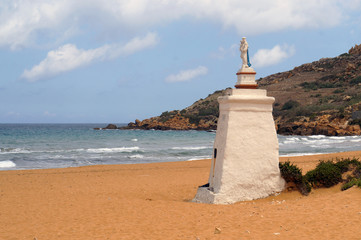 Saint Mary figure on red sandy beach in Ramla Bay, Gozo, Malta