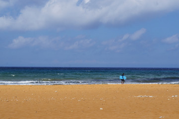 Fototapeta na wymiar Lonely surfer on red sandy beach in Ramla Bay, Gozo, Malta