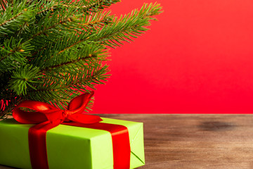 Christmas composition. Green gift box under the Christmas tree on a wooden table near a red background. a Christmas gift