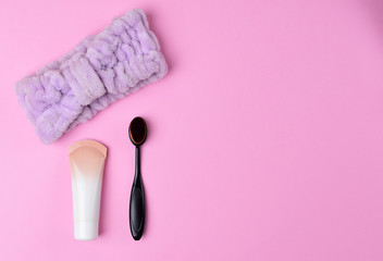 Cosmetics and accessories on a pink background. Black makeup brush, foundation and purple headband on a pink background. flat lay.
