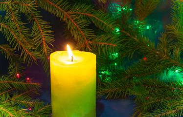 Fototapeta na wymiar Candle and Christmas branches. Bright lights of a garland. Christmas background