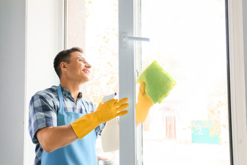 Young man cleaning window at home