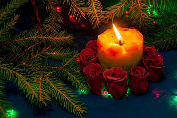 Candle with decorative roses among the branches of a Christmas tree and glowing lights. Background for New Year and Christmas. Postcard