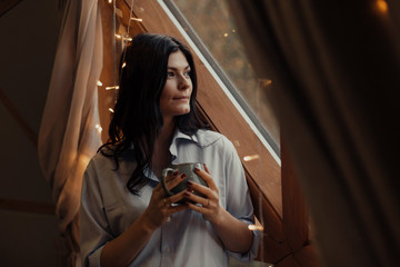 A woman in a shirt is drinking coffee by the unusual window.