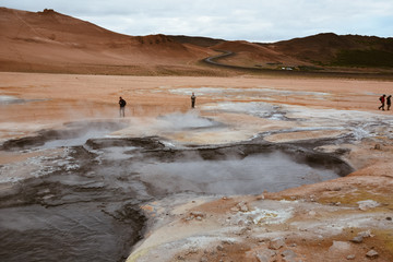 Boiling mudpots in the geothermal area Hverir and cracked ground around with unrecognisable tourists, Iceland in summer. Myvatn region, North part of Iceland